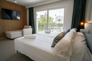 A hotel room with a bed, a sofa, a TV mounted on the wall, and a view of the city through the window. - INN Mallorca Aparthotel (Calvia)