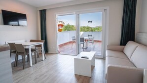 A modern living room with a sofa, a coffee table, and a dining area with chairs and a table. - INN Mallorca Aparthotel (Calvia)
