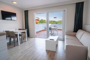 A modern living room with a sofa, a coffee table, and a dining area with chairs and a table. - INN Mallorca Aparthotel (Calvia)