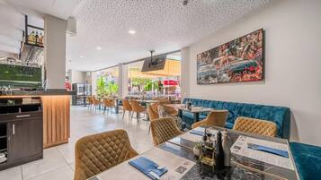 Un restaurant moderne doté d’un bar, de tables et de chaises confortables, et d’un grand tableau accroché au mur.