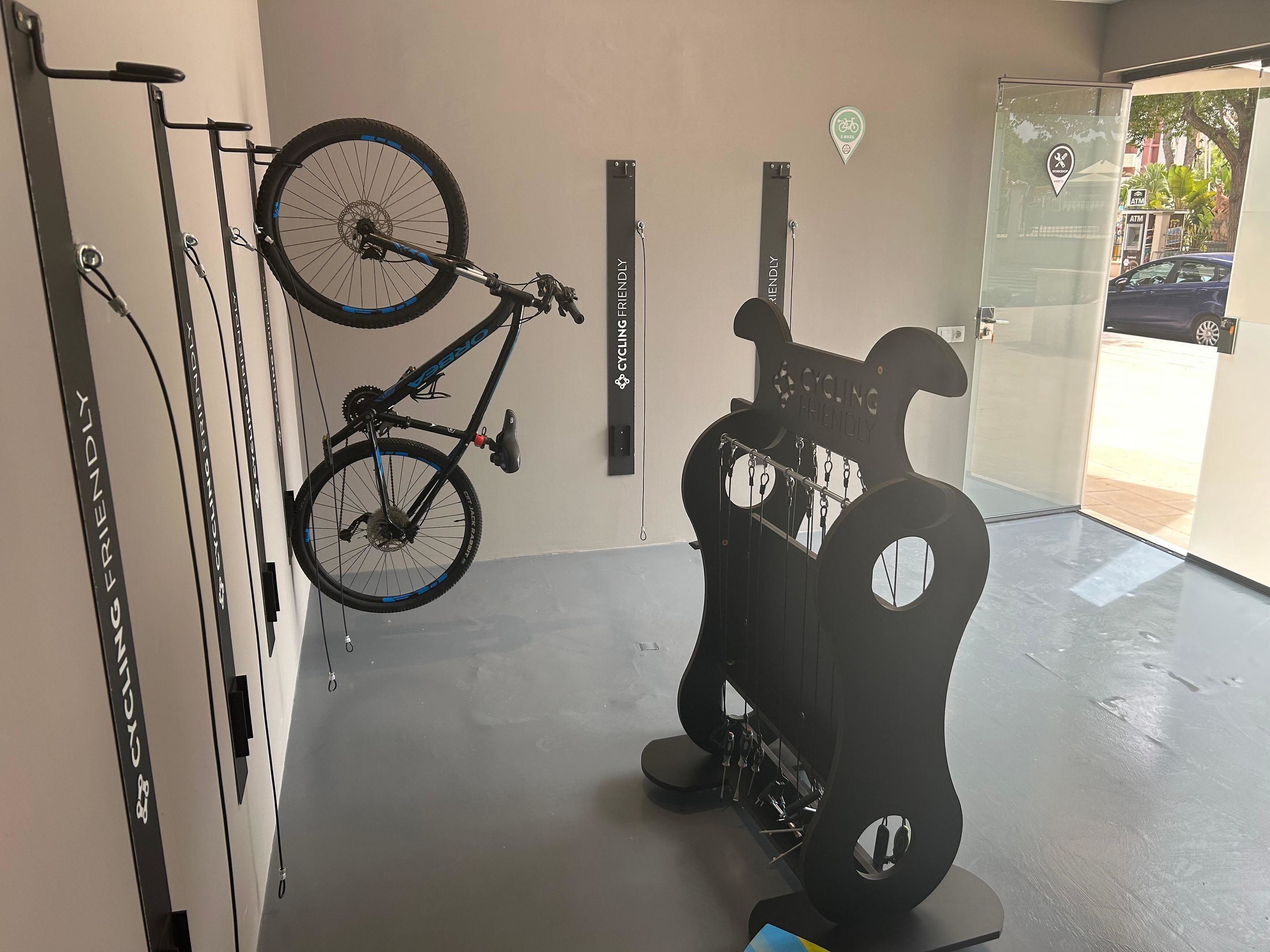 Una bicicleta colgada en un soporte de pared, un atril para reparación de bicicletas y una puerta con el símbolo de una bicicleta.
