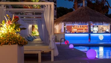 A poolside bar area with a thatched roof, seating, and a pool with illuminated spheres.