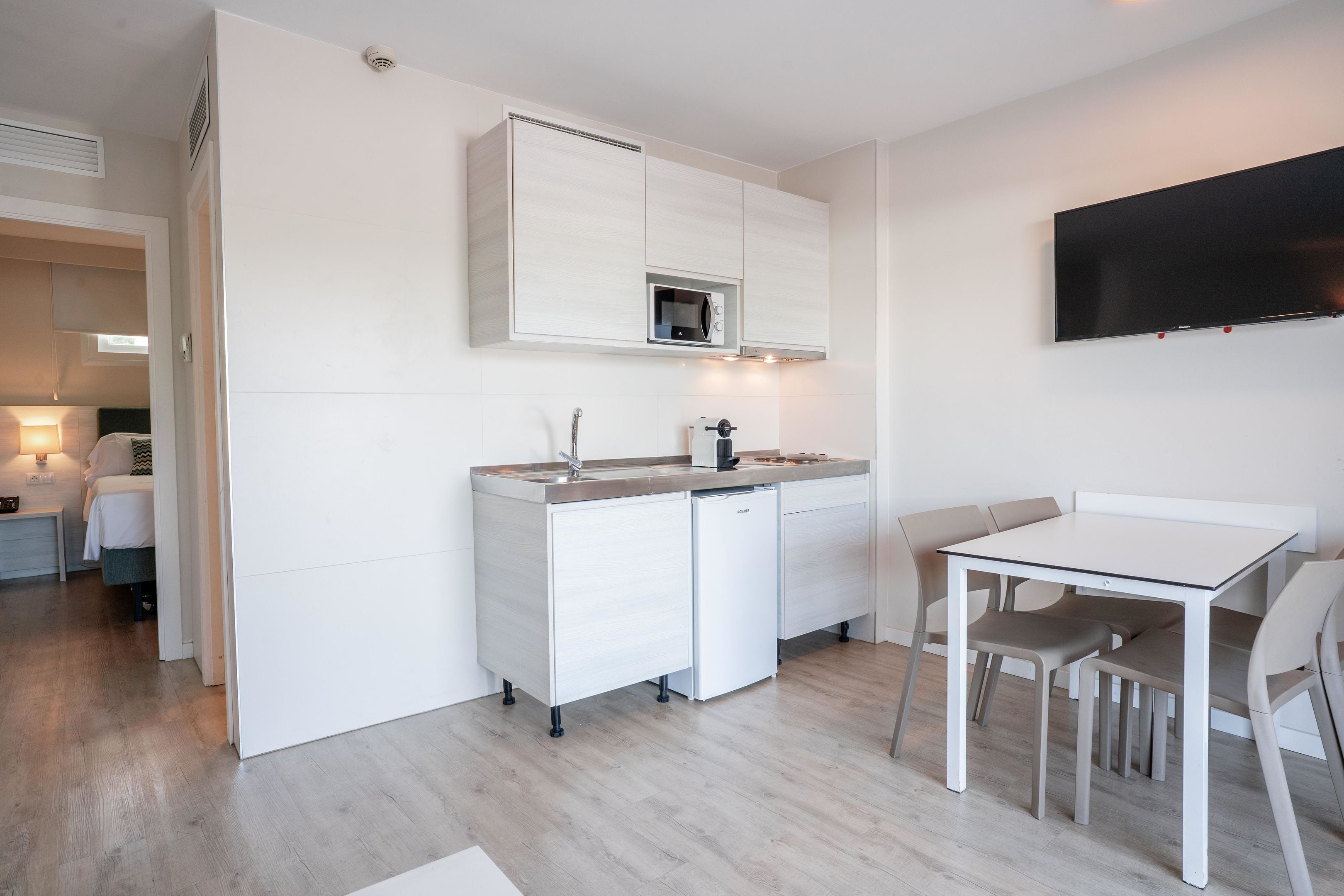 Una cocina moderna con armarios blancos, un microondas integrado y un televisor de pantalla plana montado en la pared.