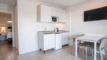 Una cocina moderna con armarios blancos, un microondas integrado y un televisor de pantalla plana montado en la pared.