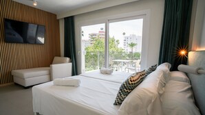 A hotel room with a bed, a sofa, a TV mounted on the wall, and a view of the city through the window. - INN Mallorca Aparthotel (Calvia)