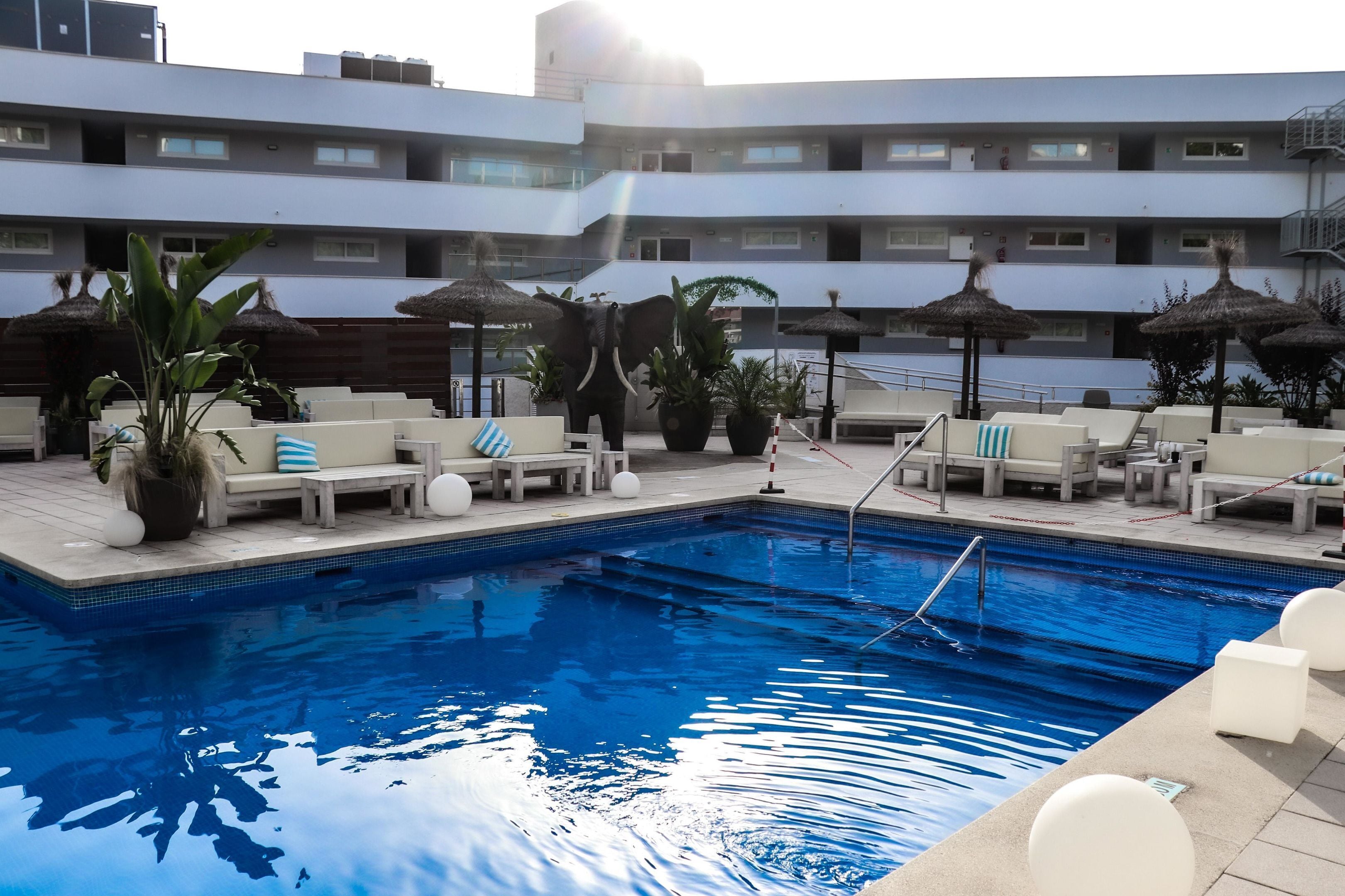A swimming pool with lounge chairs and umbrellas, surrounded by a multi-story hotel building.