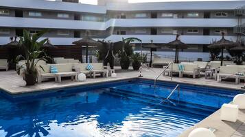 A swimming pool with lounge chairs and umbrellas, surrounded by a multi-story hotel building.