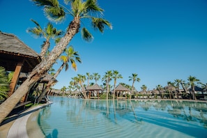 A resort pool with palm trees, thatched-roof huts, and lounge chairs. -  Alannia Costa Blanca Resort (Crevillente)