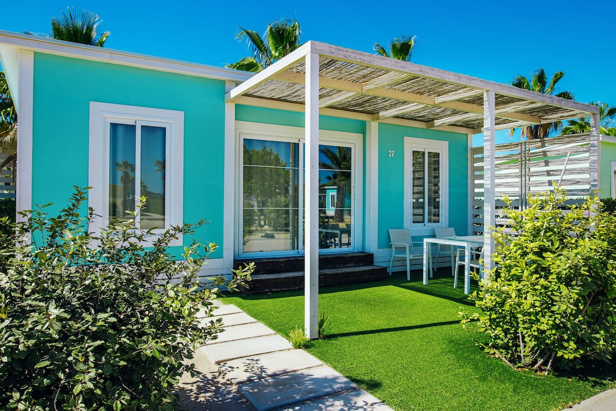 A modern house with a turquoise exterior, white windows, and a covered patio area.