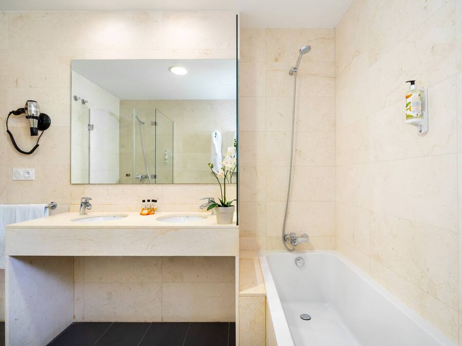 A bathroom with two sinks, a large mirror, a shower, and a hairdryer on the wall.