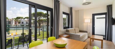 A modern living room with a dining area, large sliding glass doors to a balcony, and a view of a residential area.