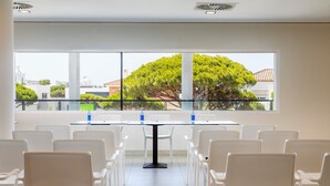 Un salón de conferencias con un ventanal grande, sillas blancas y una mesa de vidrio.