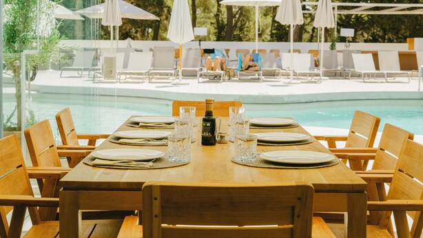 A wooden dining table set for six with a view of a pool and lounge chairs. - Ses Eufabietes Apartments & Restaurant (Formentera)