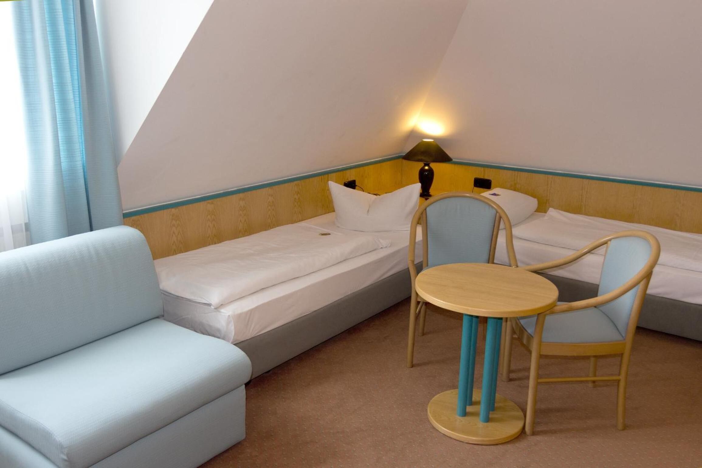 Una habitación pequeña y acogedora con una cama individual, un sofá y una mesa con dos sillas.
