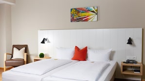 A hotel room with a large bed, two bedside tables, a chair, and a colorful artwork on the wall. - Hotel Alpha (Nuremberg)