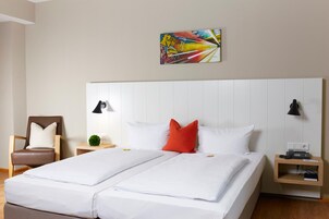 Habitación de hotel con una cama grande, dos mesitas de noche, una silla y una obra de arte colorida en la pared.