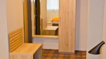 A hotel room with a bed, a bench, a mirror, a wardrobe, and a small table.