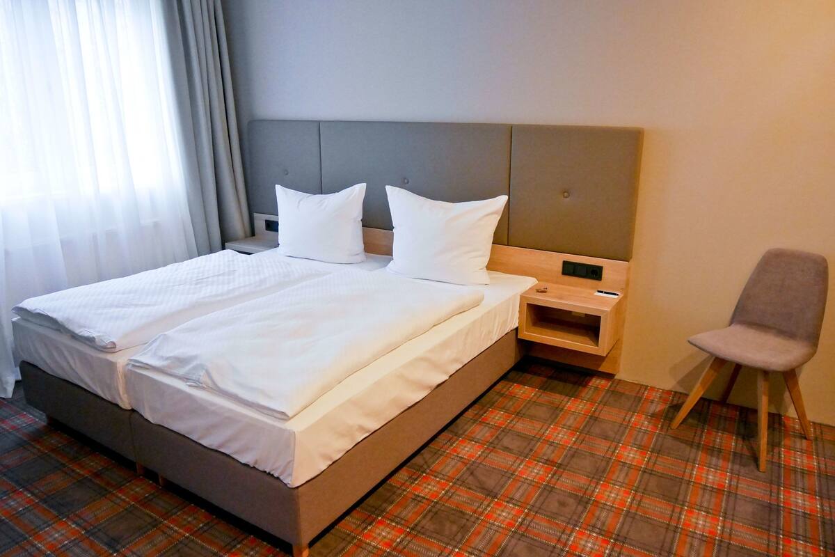 Una habitación de hotel con cama, mesita de noche, una silla y suelo estampado de pata de gallo.