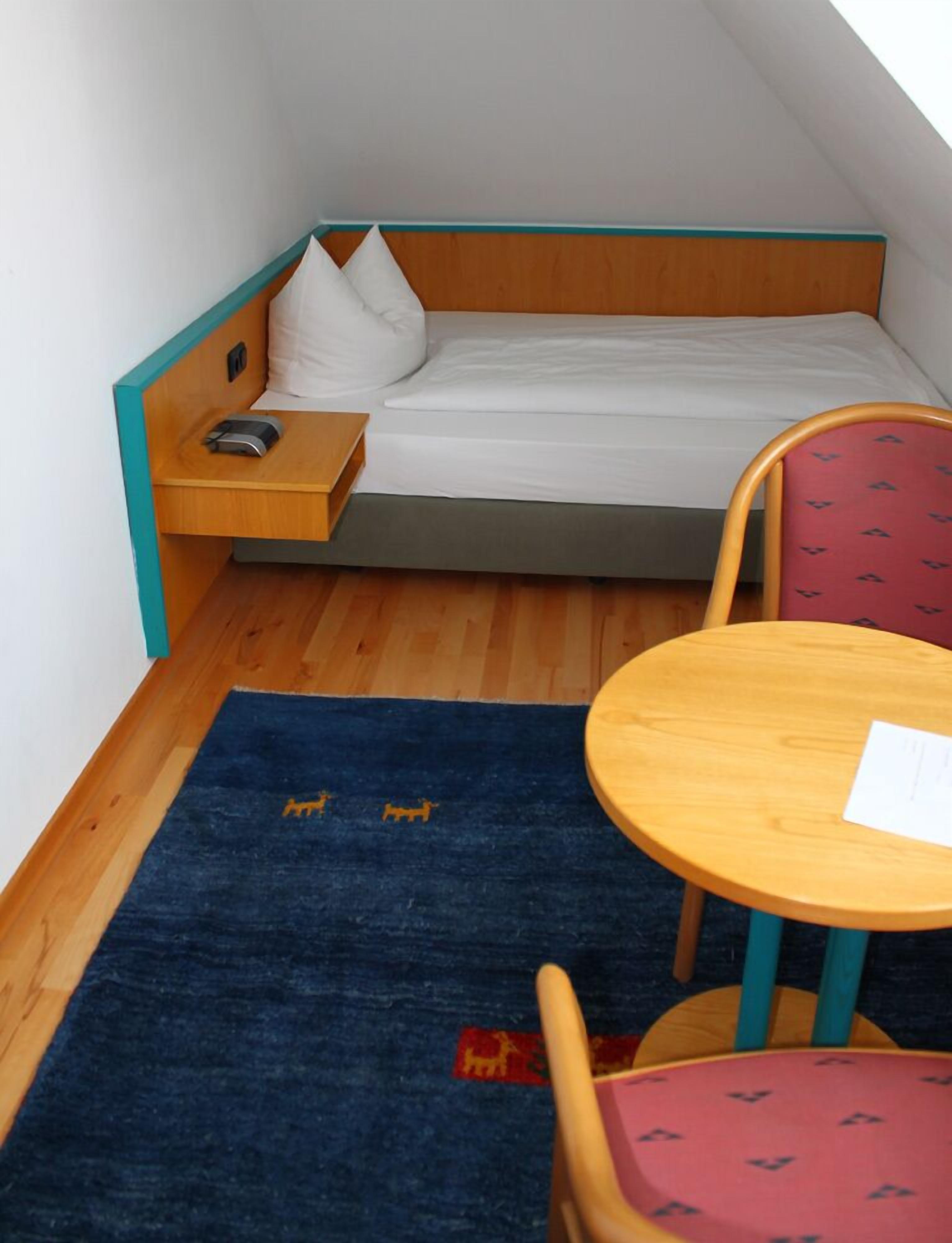 A small, compact room with a bed, a desk, a chair, and a small table.