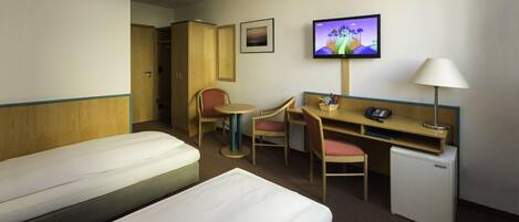 Habitación de hotel con dos camas, un escritorio con silla, televisión y un refrigerador pequeño.