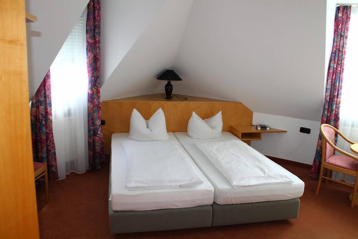 Una cama con dos camas individuales, cabecera de madera, mesita de noche con lámpara y una silla.