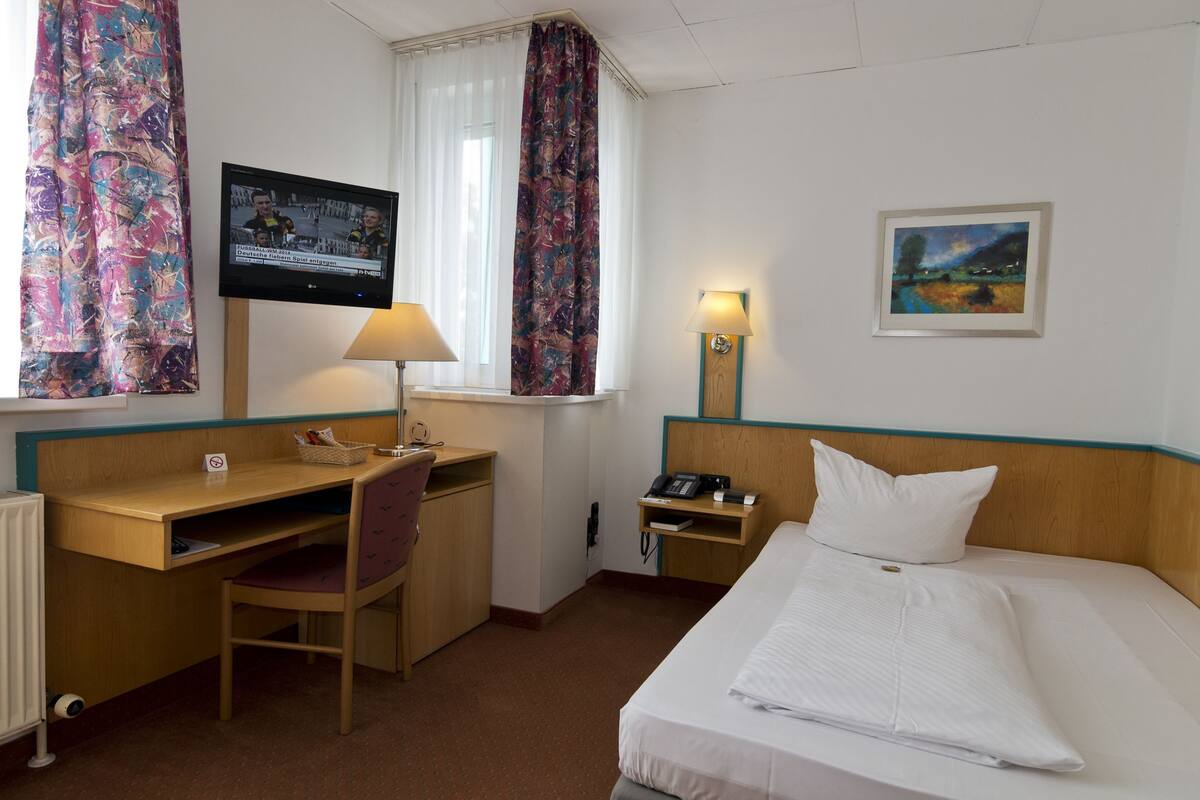 Habitación de hotel con cama, escritorio, silla, televisor, lámpara y obras de arte.