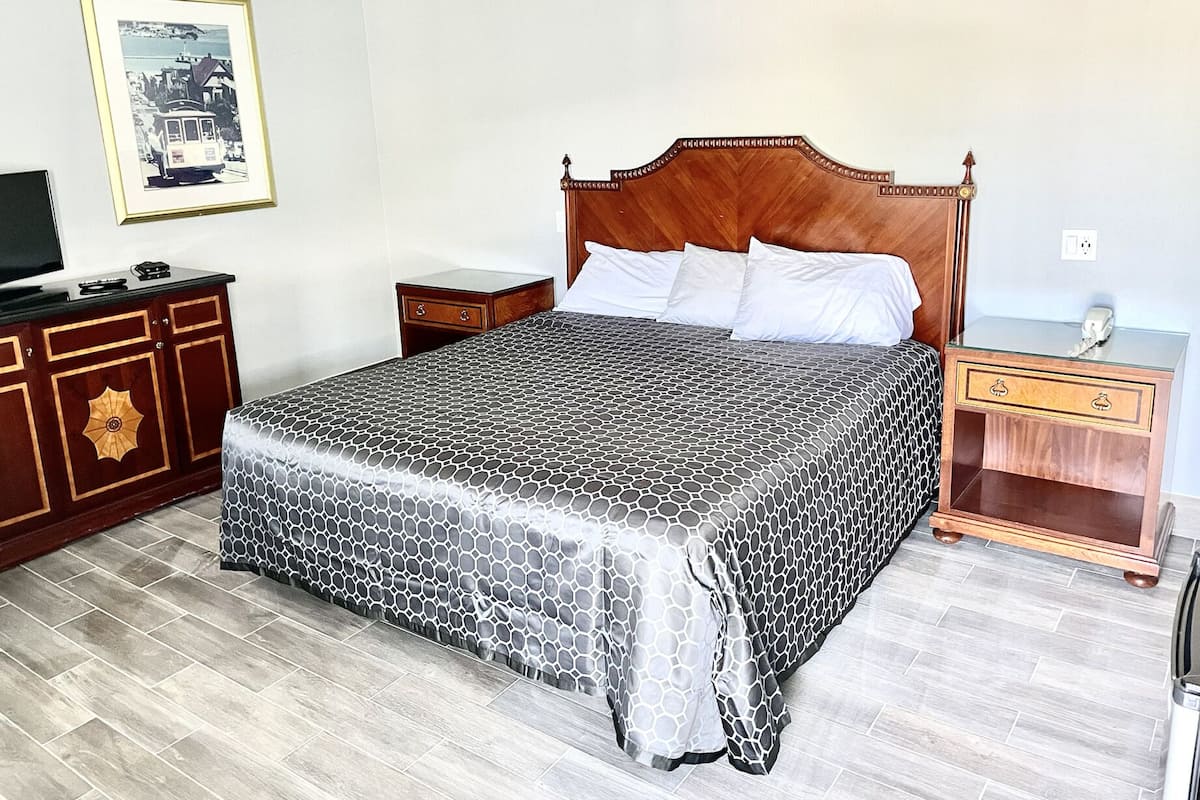 A neatly arranged bedroom with a large bed, a wooden nightstand, a dresser, and a television on a cabinet.