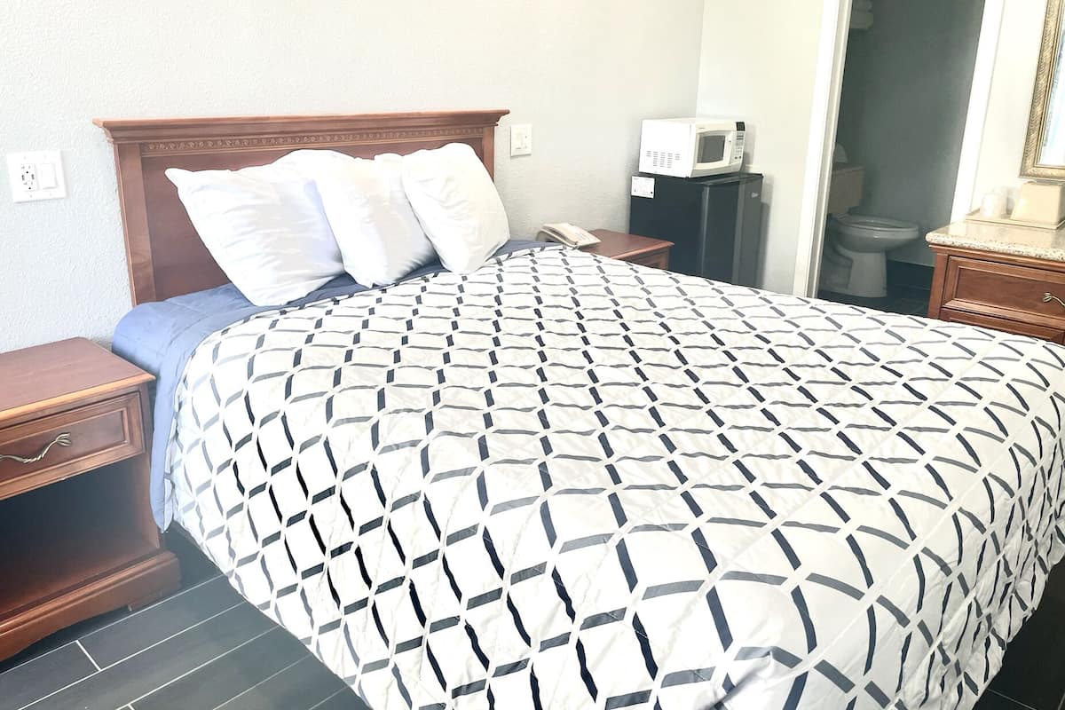 A hotel room with a bed, a nightstand, a bedside table, a microwave, and a bathroom visible through an open door.