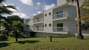Un bâtiment moderne à plusieurs étages, doté de fenêtres rondes et de balcons, entouré de verdure et de palmiers.