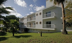 A modern multi-story building with circular windows and balconies, surrounded by greenery and palm trees.