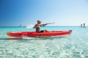 A person kayaking on clear turquoise water with a sailboat in the background. - Es Pi2 (Formentera)