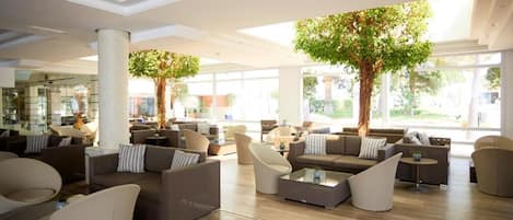 A spacious lobby with modern furniture, large windows, and indoor trees.