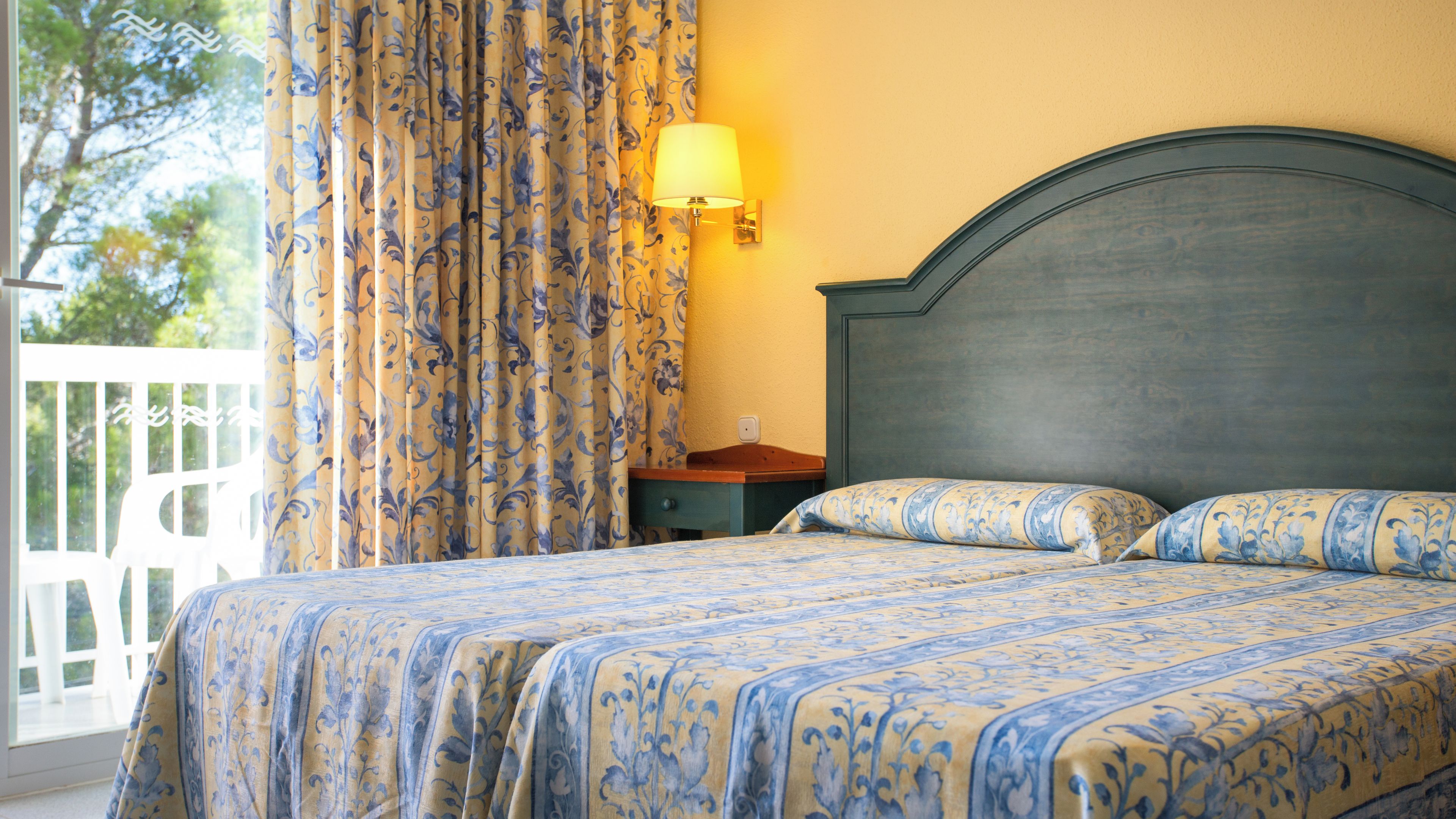 Een bed met een bloemenprint, een nachtkastje, een lamp en uitzicht op het landschap.