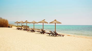 A beach with rows of sun loungers and thatched umbrellas.