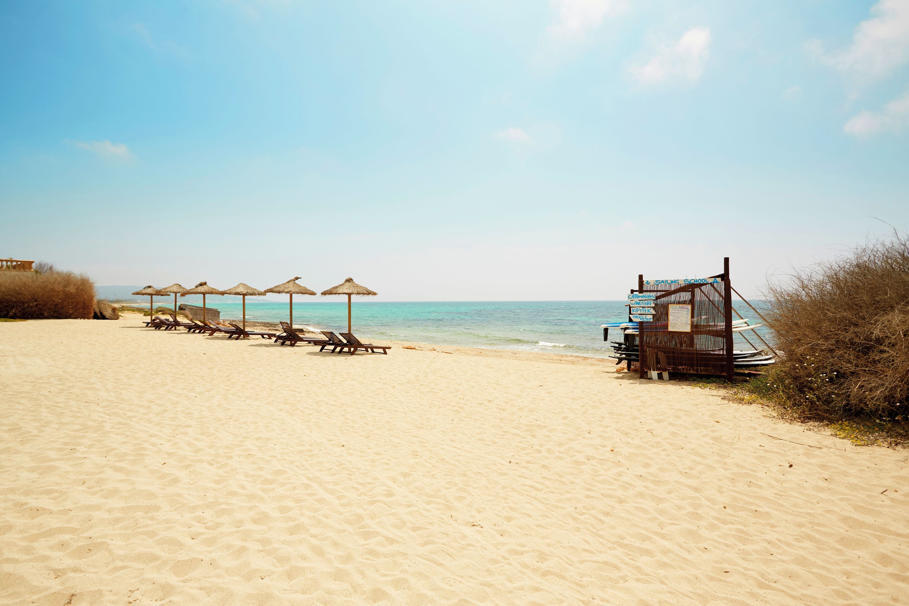 A beach with sun loungers and umbrellas, a lifeguard tower, and the ocean in the background.