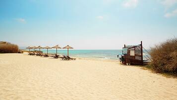 A beach with sun loungers and umbrellas, a lifeguard tower, and the ocean in the background.