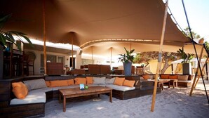 A covered outdoor seating area with sofas and a wooden table, surrounded by sand. - Es Pi2 (Formentera)