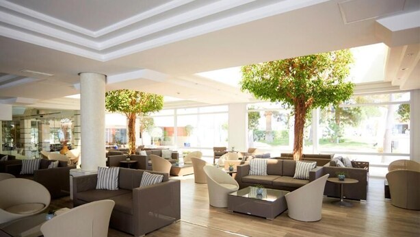 A spacious lobby with modern furniture, large windows, and indoor trees. - Es Pi2 (Formentera)