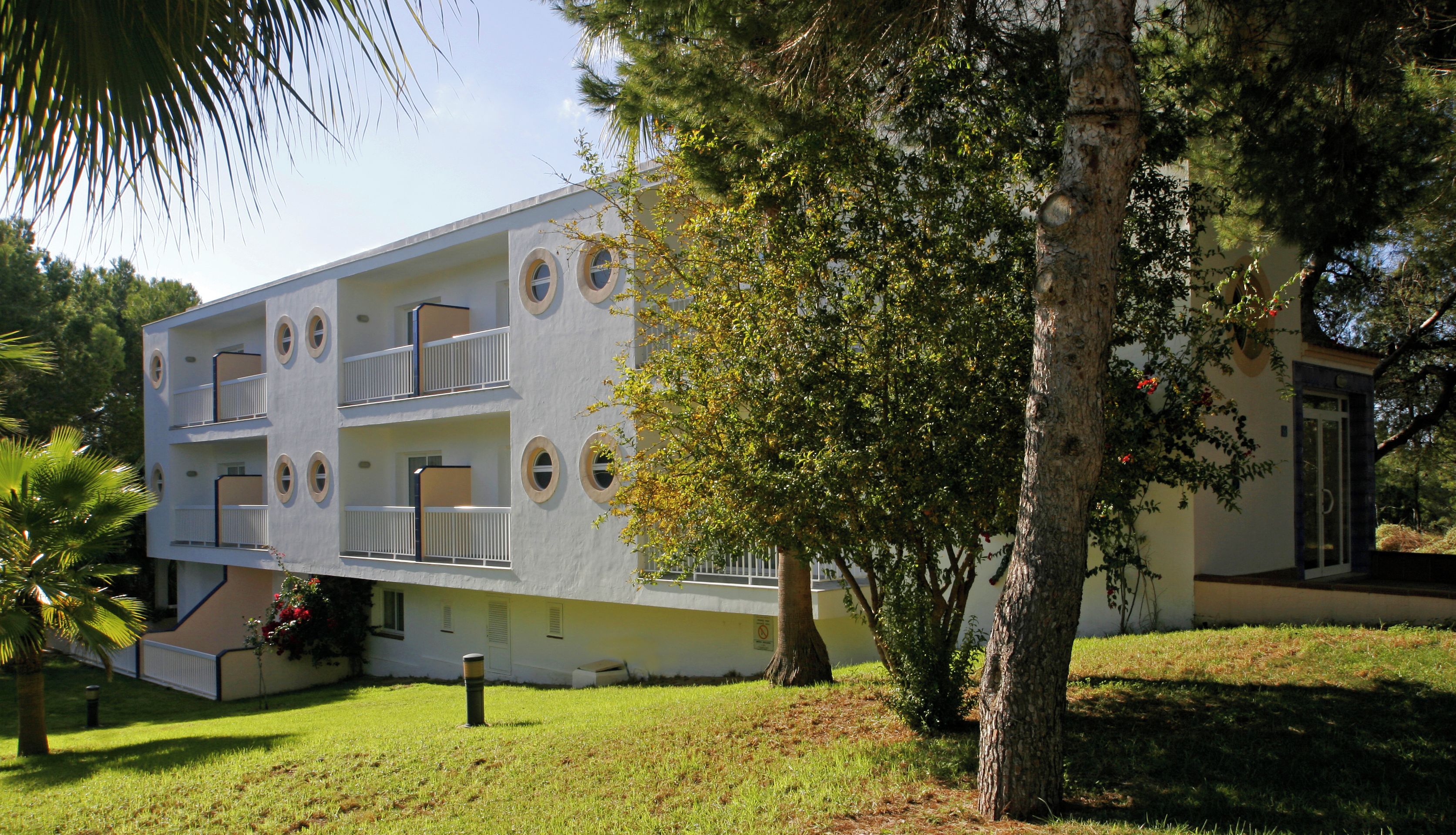 A multi-story building with balconies, surrounded by trees and grass.