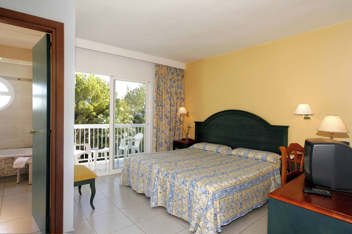 A bedroom with a bed, a television, and a balcony with chairs.