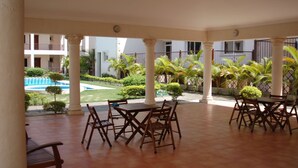 A covered outdoor area with a pool, palm trees, and a building in the background. - Bavaro Green (Punta Cana)