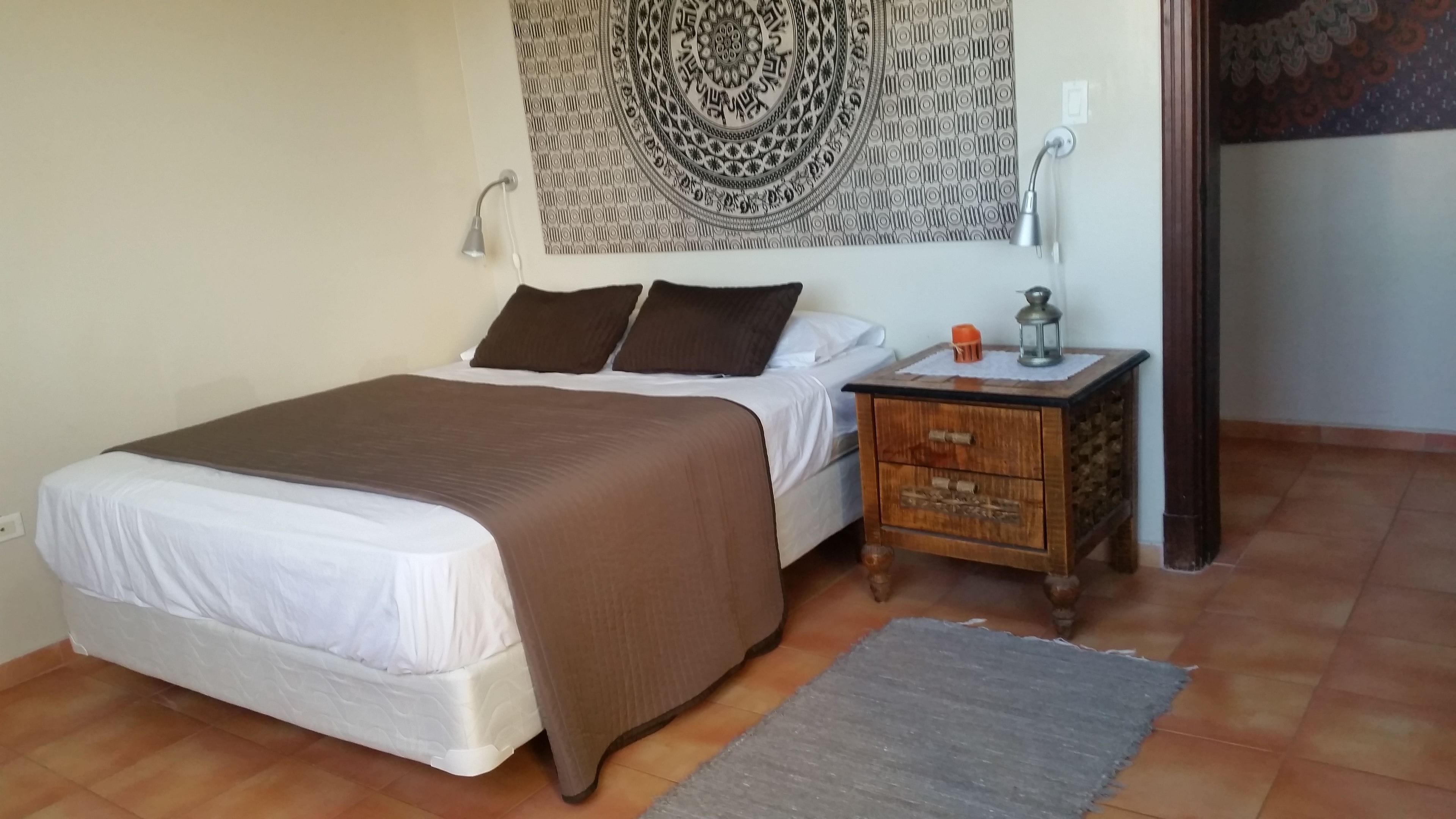 A bedroom with a bed, a nightstand, a lamp, and a patterned tapestry on the wall.