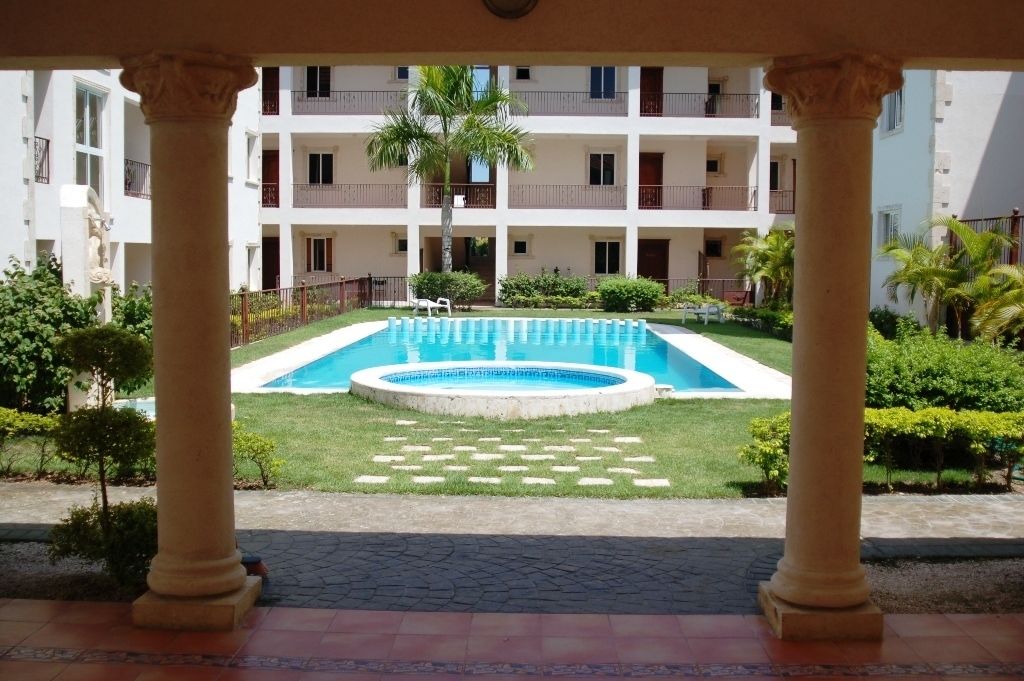 Un patio con piscina, rodeado por un edificio de varios pisos con balcones.