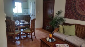 A living room with a wooden sofa, a dining table set with plates and bowls, and a large potted plant. - Bavaro Green (Punta Cana)