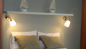 A bed with two pillows, two wall-mounted lamps, and two small sailboat models on a shelf above. - Bavaro Green (Punta Cana)