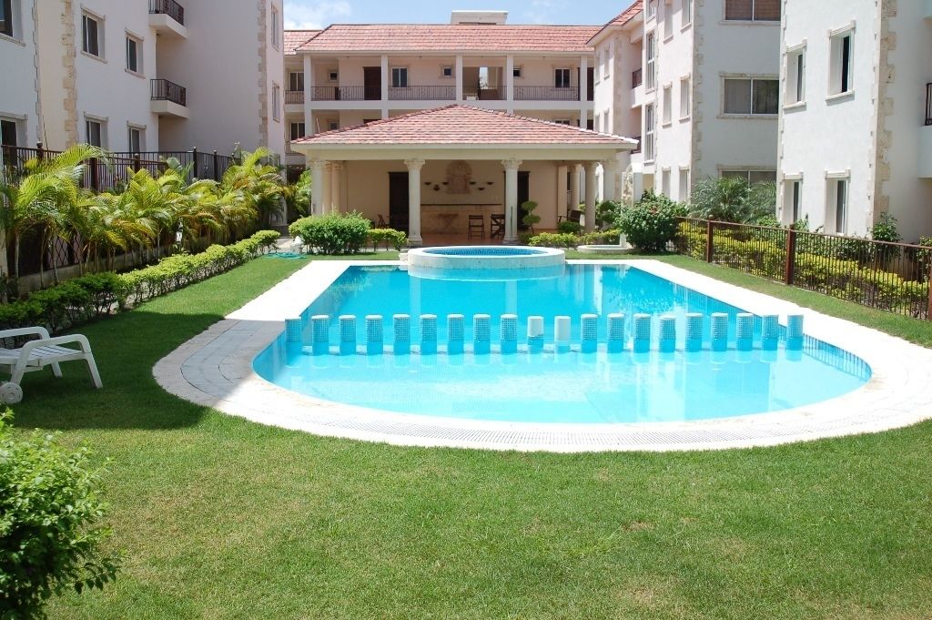 A swimming pool surrounded by a well-maintained lawn, with a building in the background.