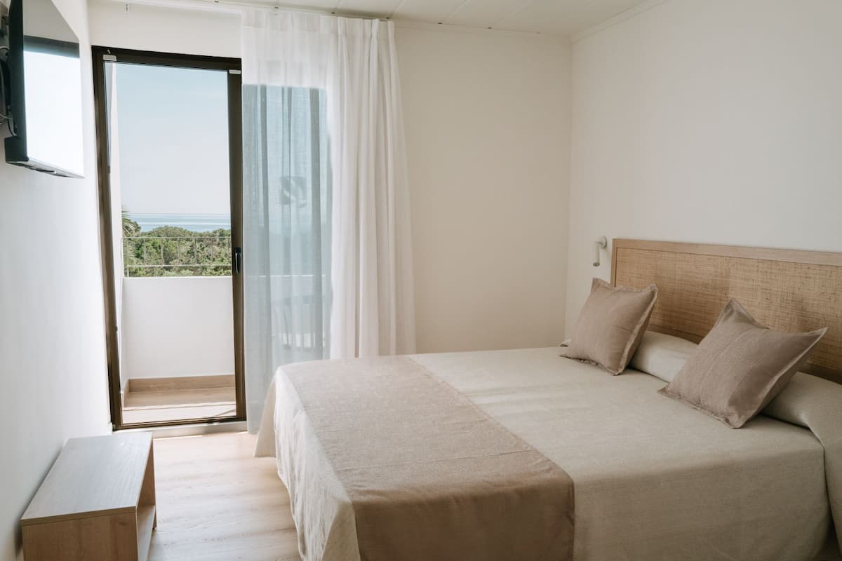 A bedroom with a bed, a wooden nightstand, a view through a glass door, and a balcony.