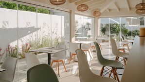 A modern dining area with glass walls, white chairs, and a table. - Hotel Rosamar (Formentera)