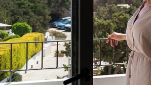 A person standing by a window with a view of the sea and greenery. - Hotel Rosamar (Formentera)