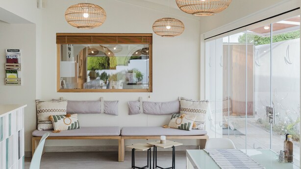 A modern living room with a wooden bench, a glass table, and wicker pendant lights. - Hotel Rosamar (Formentera)